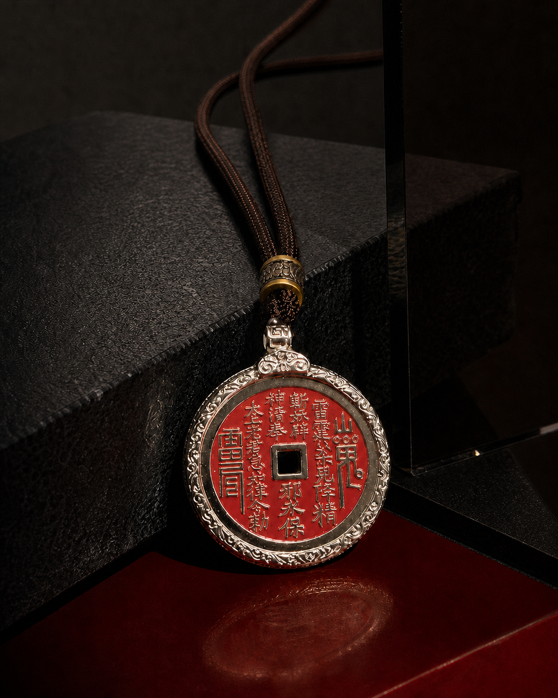 SHAN GUI Vermilion Guardian necklace resting against dark stone above a red lacquer surface.