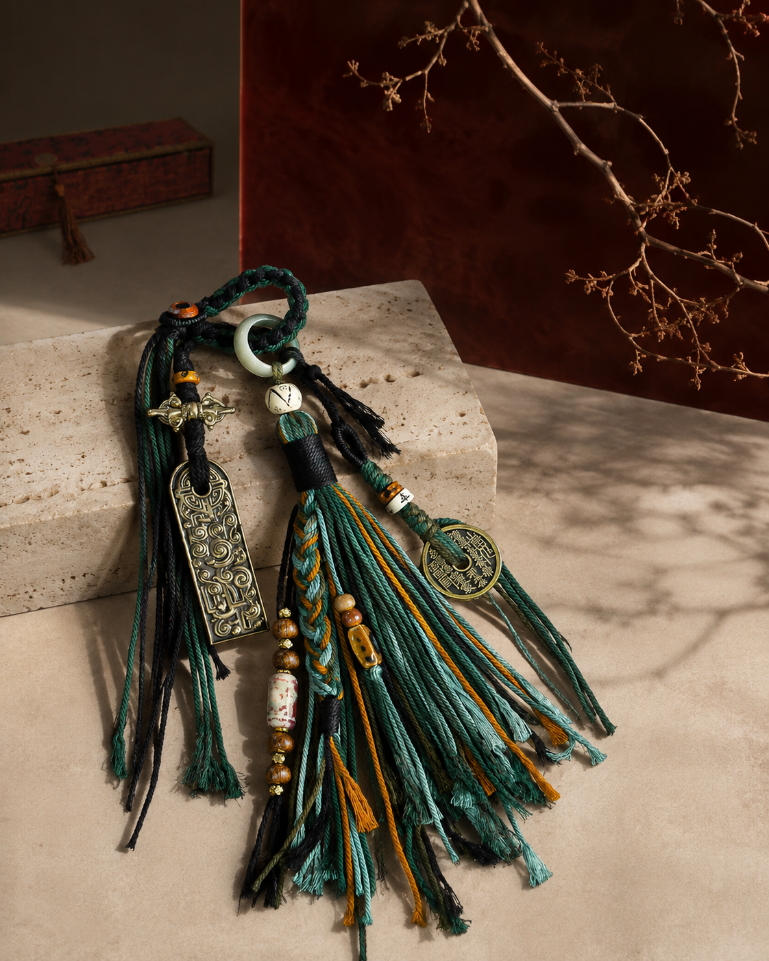 Forest tassel charm arranged on pale stone against an oxblood backdrop.